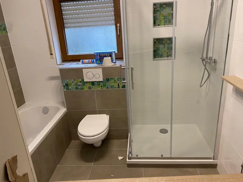 Renoviertes Badezimmer mit Badewanne, Dusche und grüner Mosaik-Bordüre